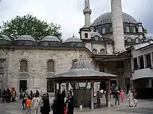 A building with several domes, large and small, in front of a courtyard with a smaller standalone structure