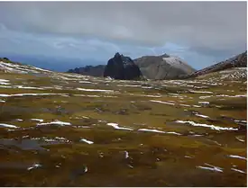  A bare stretch of land with ice and snow patches, leading to rocky hills in the background