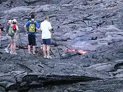 溶岩流を棒で突いて観察する観光客。