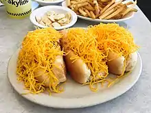 small oval white plate with cheese coney showing bun, hot dog, sauce, and shredded cheese