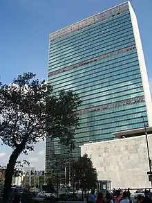 Picture of a tall building with a tree in front of a blue sky.