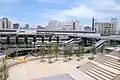 （画像1）宇都宮駅東口駅前広場（宮みらいライトヒル「水のテラス」）と広場を横切る電車