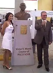 Photograph of two persons in front of a sculpture